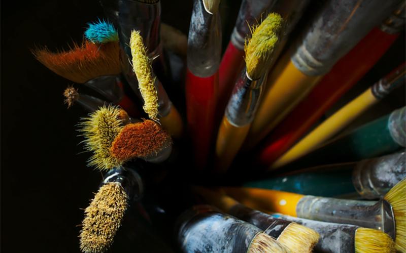 close up image of used paint brushes coated in various colors of paint