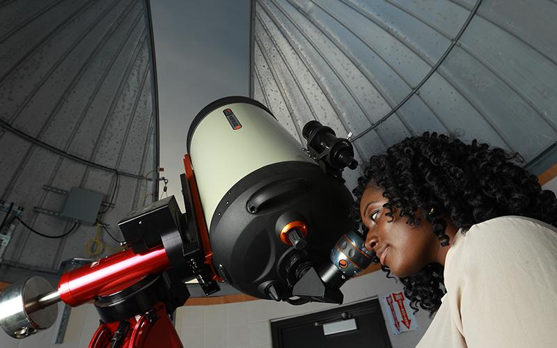 woman looking through a telescope at the sky in an observatory