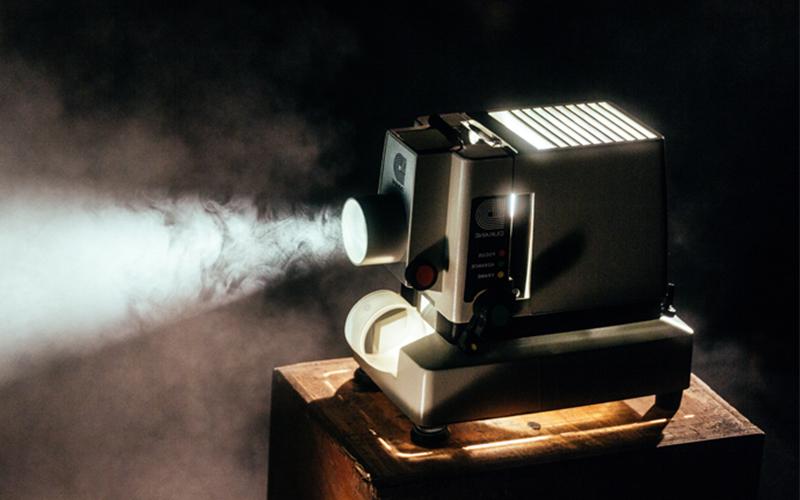 film projector sits on a stand projecting light from its lense in a darkened room