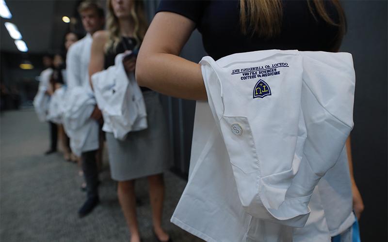 row of medical school graduates holding their UToledo College of Medicine white coats