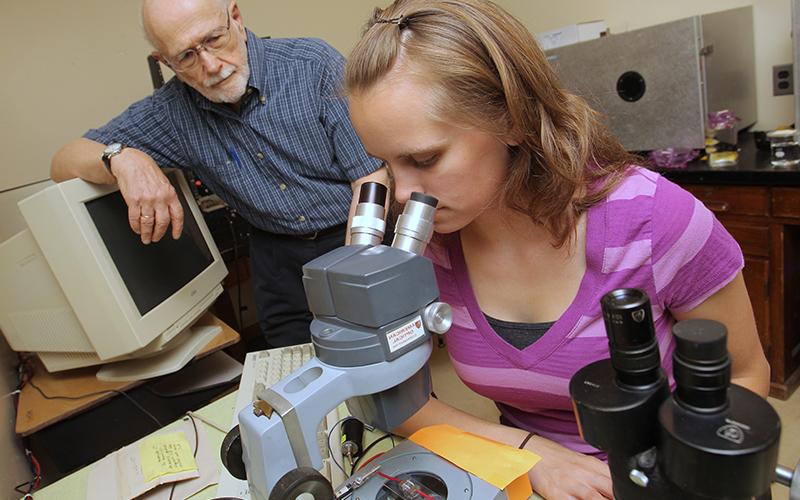 woman observes sample under a microscope in a lab 