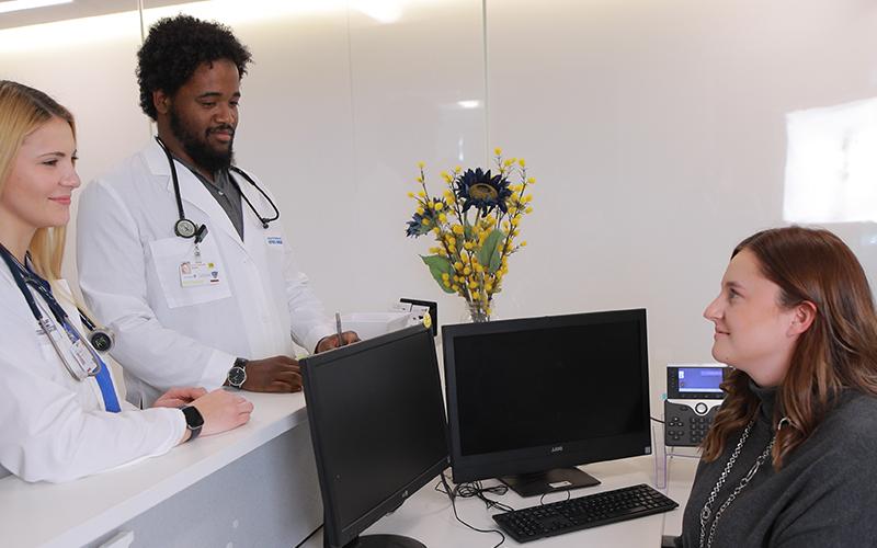 two doctors in white coats talk to receptionist sitting at her desk