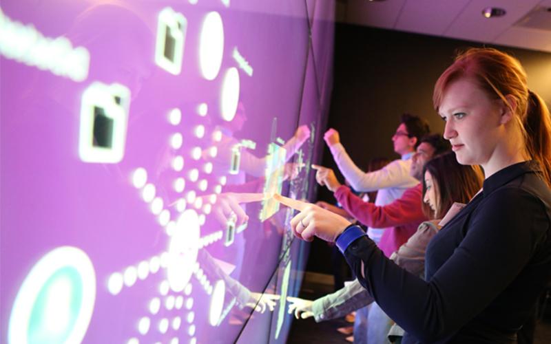 line of students interact with a purple touch screen featuring various elements and buttons