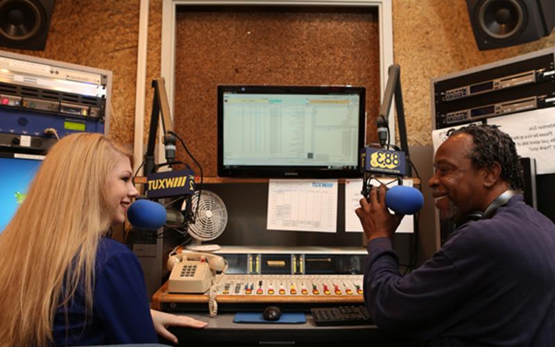 two UToledo radio hosts sit in front of microphones in their radio station