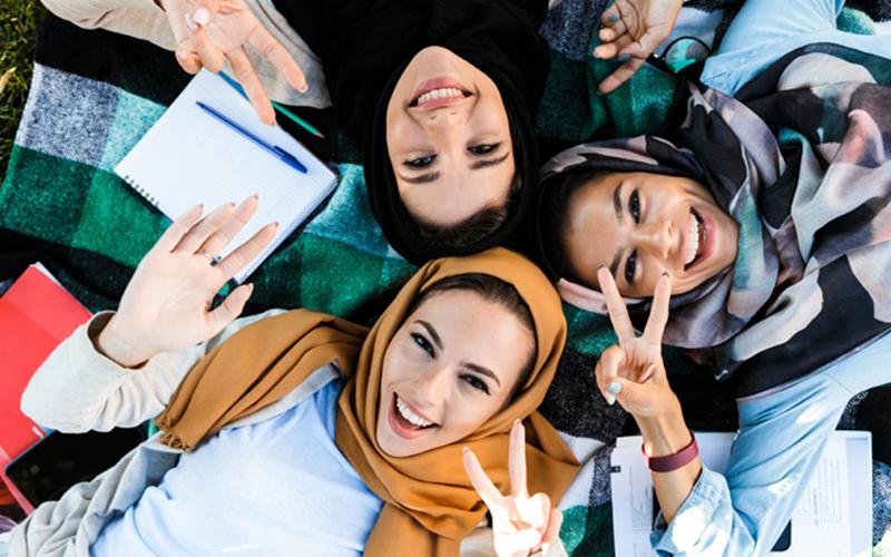 ariel view of three religious studies students smiling and posing with the peace sign to the camera