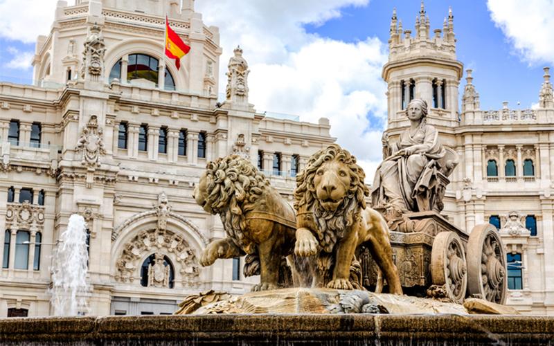 spanish architechture featuring a fountain and flag of Spain waving in the wind