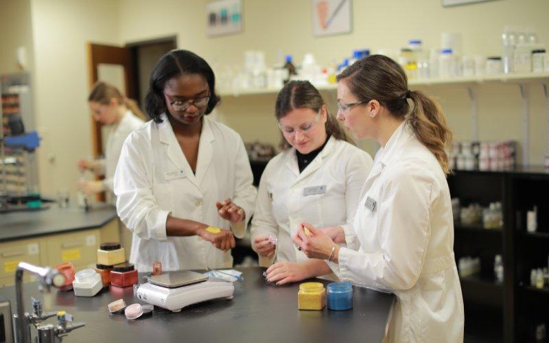 three pharmacy students wearing white lab coats in a pharmacy lab