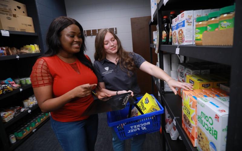 two women pick out groceries from a shelf in a food pantry